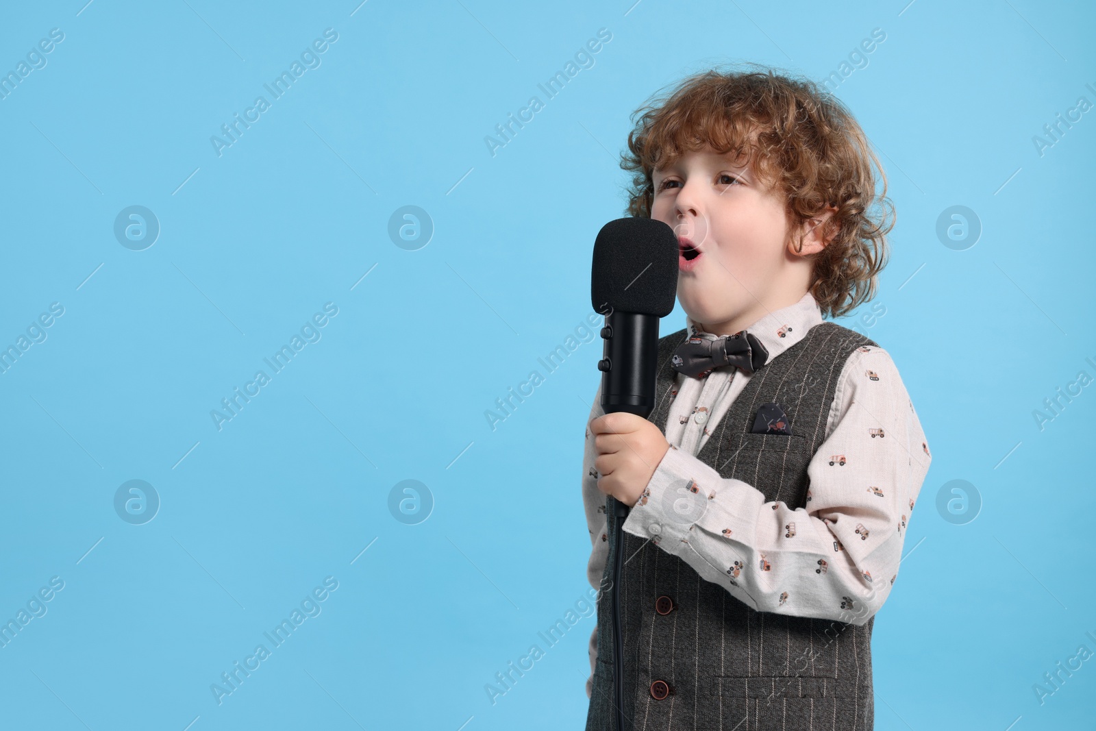 Photo of Cute little boy with microphone singing on light blue background, space for text