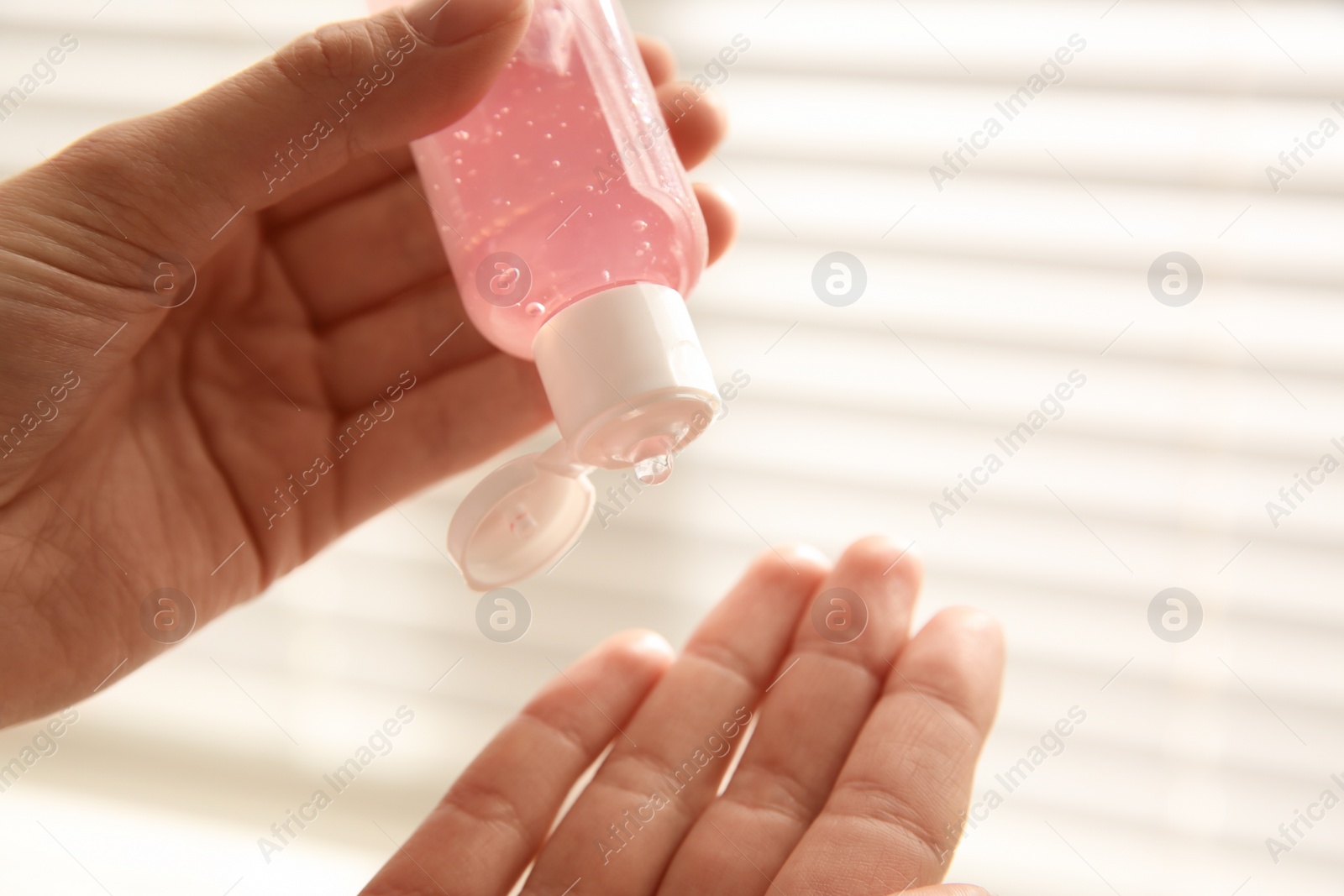 Photo of Woman applying antiseptic gel near window indoors, closeup