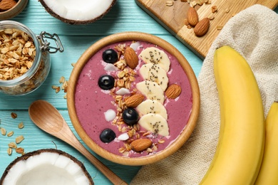 Photo of Delicious acai smoothie with granola and almonds served on light blue wooden table, flat lay