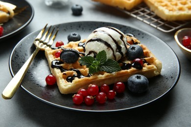 Photo of Delicious Belgian waffle with ice cream, berries and chocolate sauce on grey table, closeup