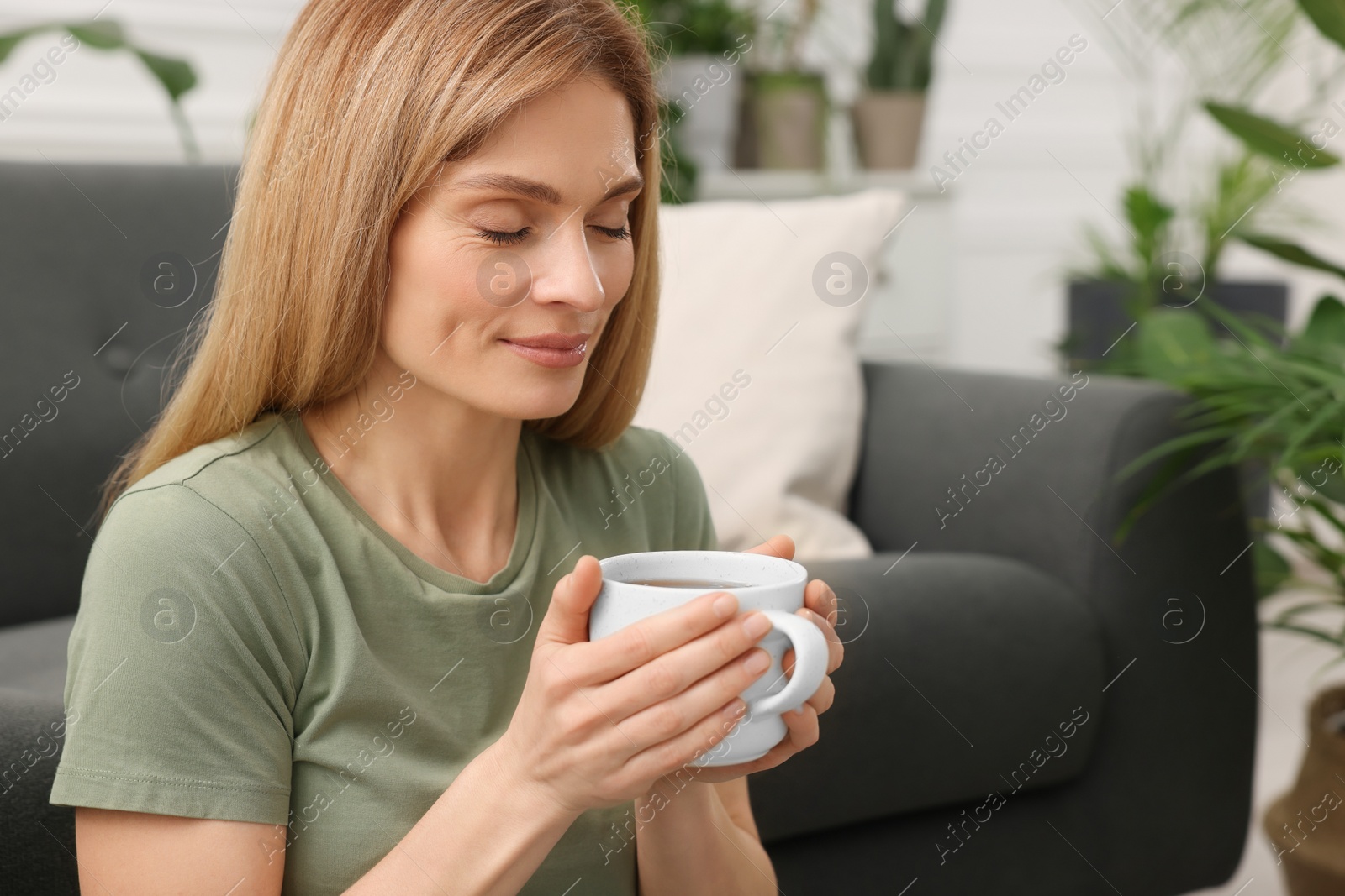 Photo of Woman holding cup of tea in room with beautiful houseplants. Space for text