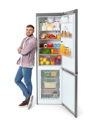 Young man near open refrigerator on white background