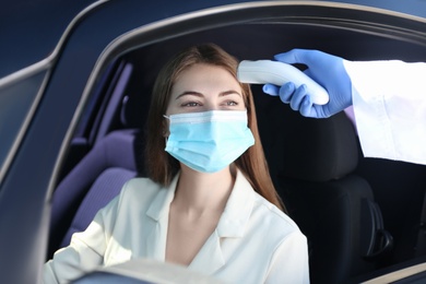 Doctor measuring woman's temperature with non contact infrared thermometer in car