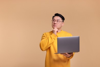 Photo of Thoughtful man with laptop on beige background, space for text