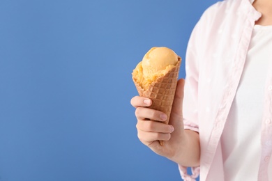 Photo of Woman holding yellow ice cream in wafer cone on light blue background, closeup. Space for text