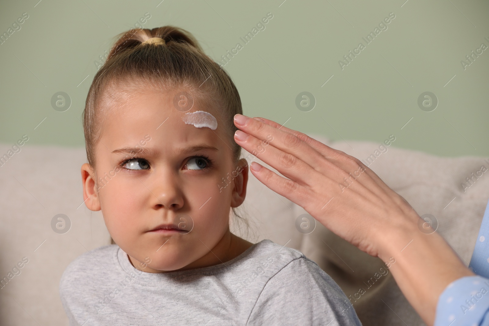 Photo of Mother applying ointment onto her daughter's forehead indoors