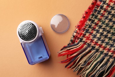 Photo of Modern fabric shaver and knitted scarf on pale orange background, flat lay