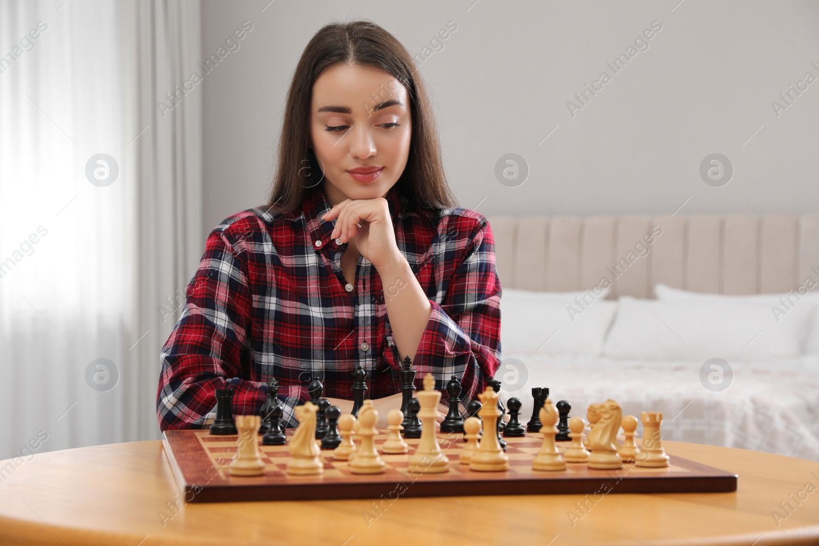 Photo of Young woman playing chess at table in bedroom