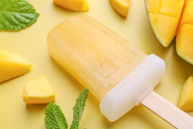 Photo of Tasty mango ice pop on light yellow background, closeup. Fruit popsicle