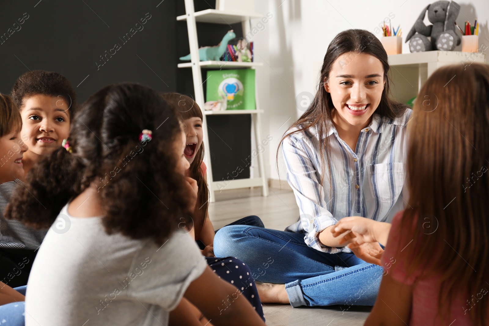 Photo of Cute little children with nursery teacher in kindergarten. Indoor activity