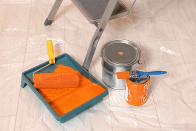 Photo of Ladder, cans of orange paint and renovation equipment on floor indoors
