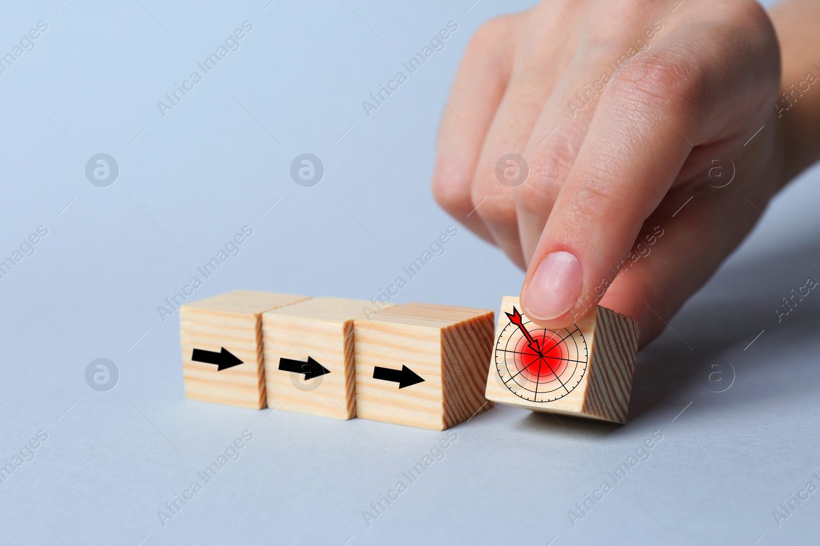 Image of Woman putting cube with icon of target into row of cubes with arrows on light background, closeup