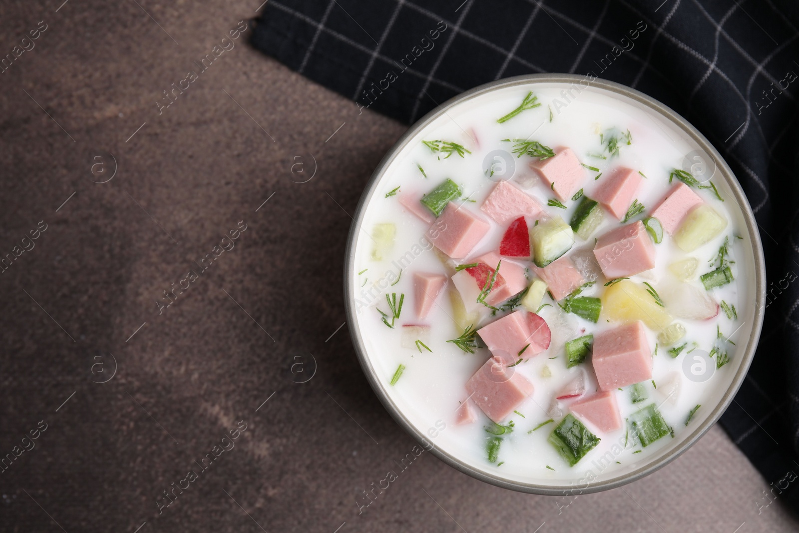 Photo of Delicious cold summer soup (okroshka) with boiled sausage in bowl on brown table, top view. Space for text