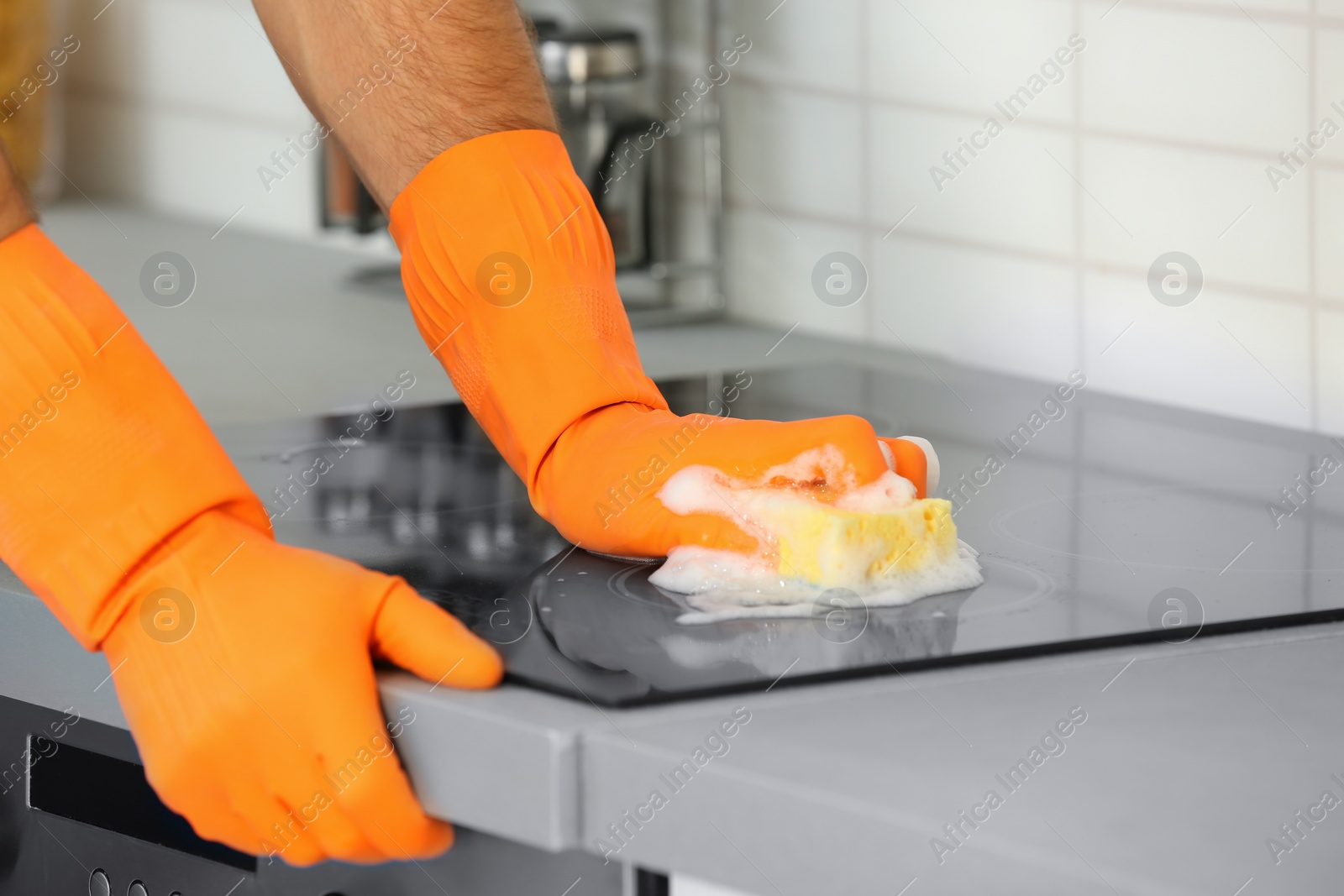 Photo of Man cleaning kitchen stove with sponge, closeup