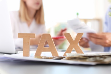 Photo of Word TAX and blurred accountants on background