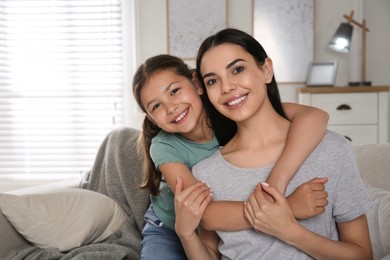 Photo of Young mother and her daughter on sofa in living room. Adoption concept