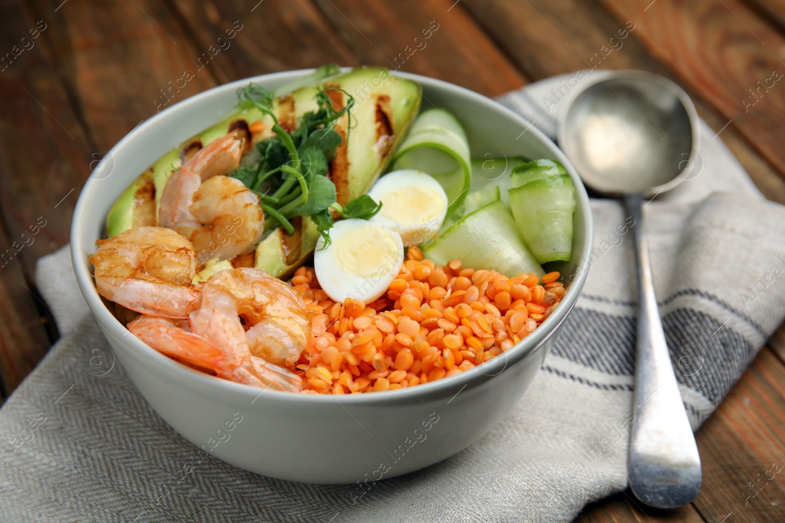 Photo of Delicious lentil bowl with avocado, shrimps, egg and cucumber on wooden table