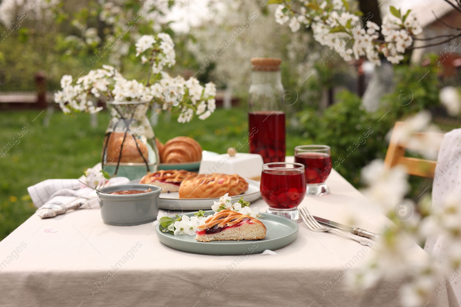 Photo of Stylish table setting with beautiful spring flowers, fruit drink and pie in garden