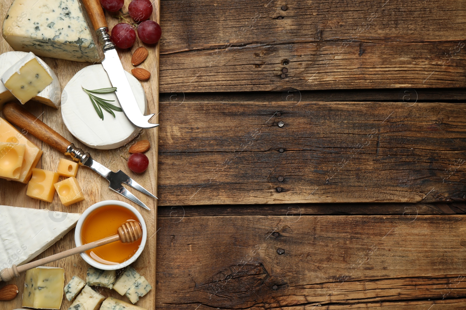 Photo of Cheese platter with specialized knife and fork on wooden table, flat lay. Space for text