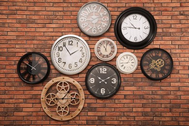 Photo of Collection of clocks hanging on red brick wall