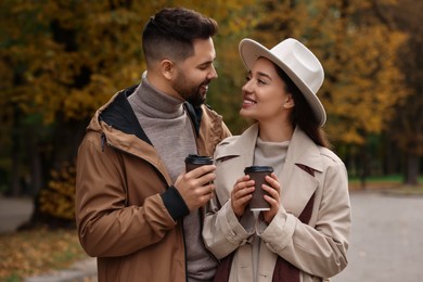 Photo of Happy young couple with cups of coffee spending time together in autumn park