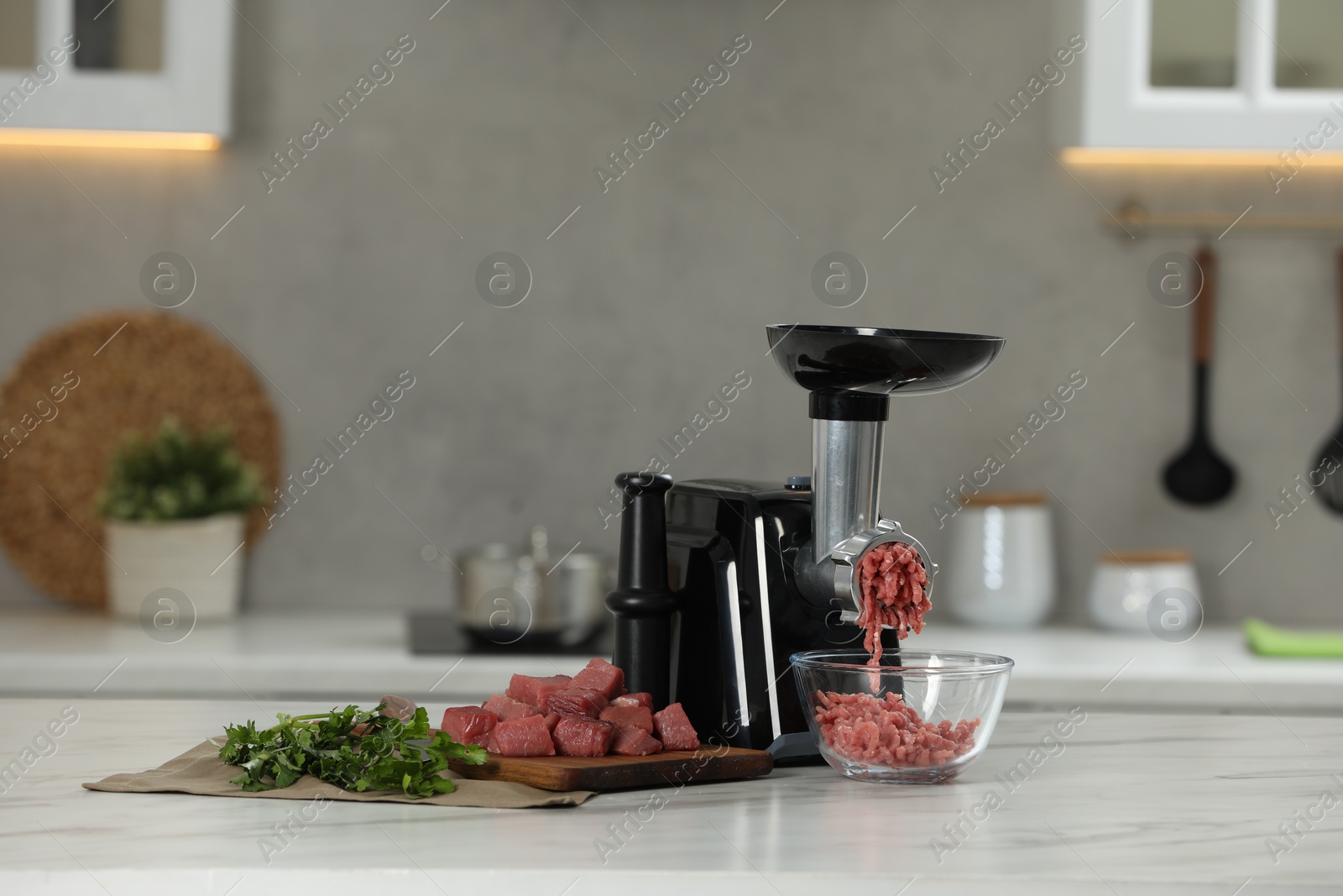 Photo of Electric meat grinder with beef mince and parsley on white table in kitchen