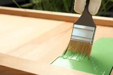 Worker applying green paint onto wooden surface, closeup. Space for text