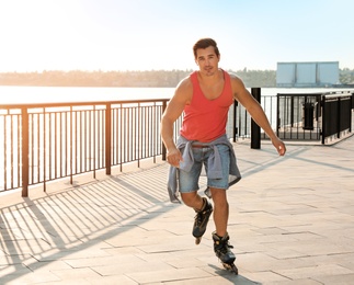 Photo of Handsome young man roller skating on pier near river, space for text