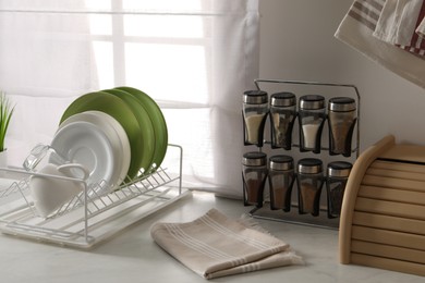 Drainer with different clean dishware, glass, cup, spices and napkin on light table indoors