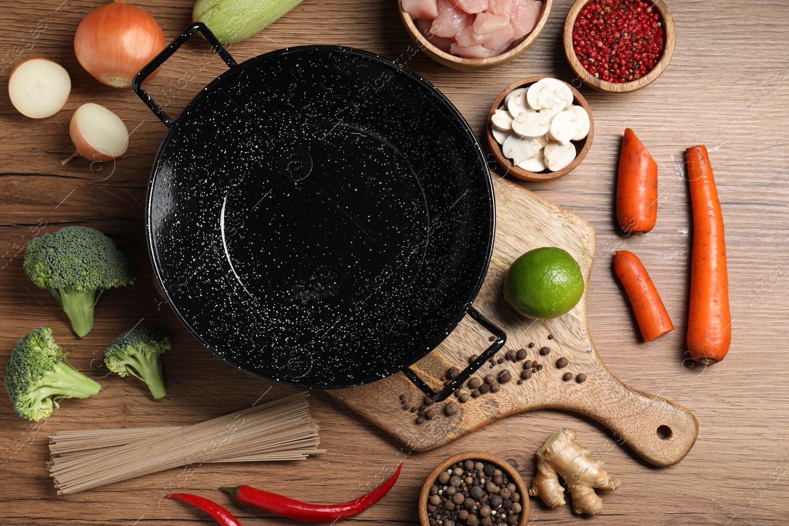 Photo of Empty iron wok surrounded by raw ingredients on wooden table, flat lay