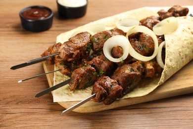 Photo of Metal skewers with delicious meat, tortilla and onion served on wooden table, closeup