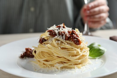 Photo of Woman enjoying tasty spaghetti with sun-dried tomatoes and parmesan cheese and wine at wooden table in restaurant, closeup. Exquisite presentation of pasta dish