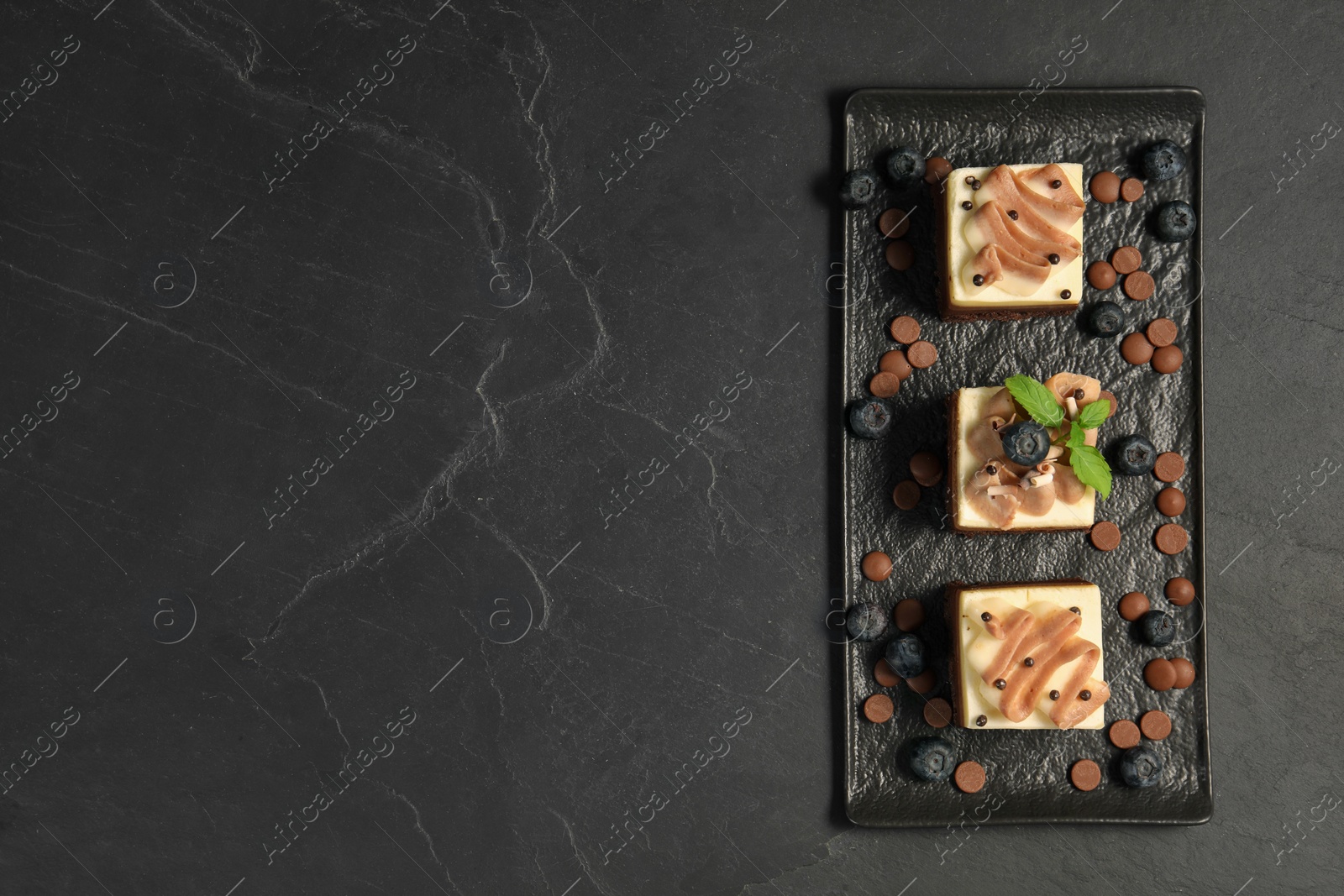 Photo of Pieces of triple chocolate mousse cake on black table, top view with space for text