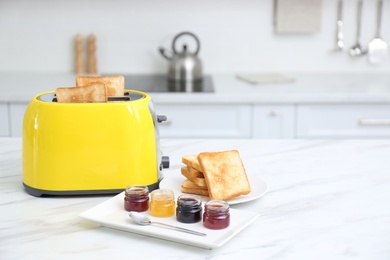 Photo of Modern toaster with slices of bread and different jams  on white marble table in kitchen, space for text