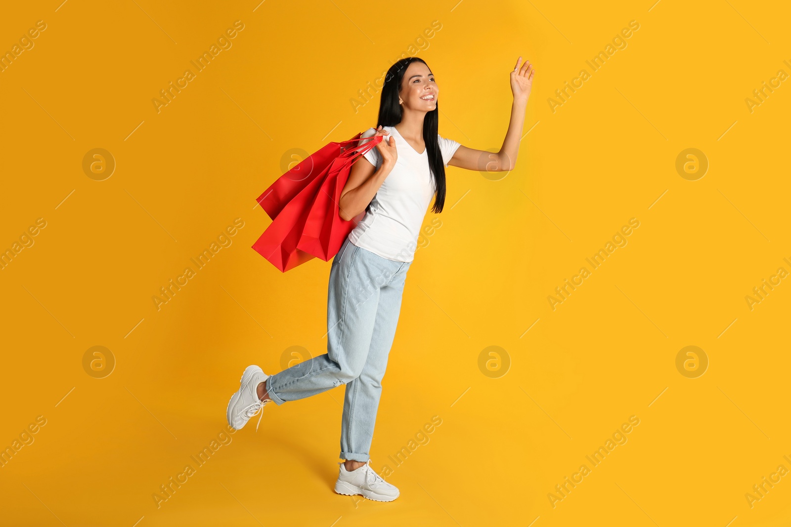 Photo of Beautiful young woman with paper shopping bags on yellow background