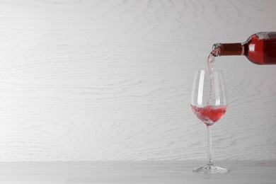 Photo of Pouring delicious rose wine into glass on table against white wooden background. Space for text