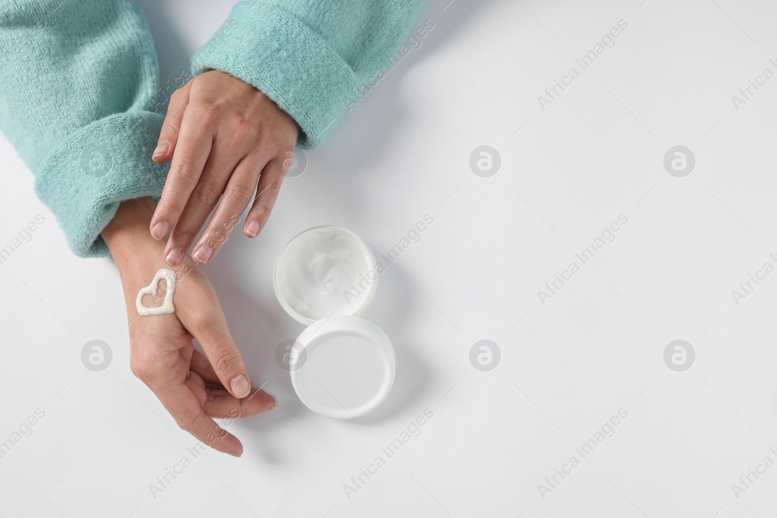 Photo of Woman with heart made of cosmetic cream on hand and jar against white background, top view. Space for text