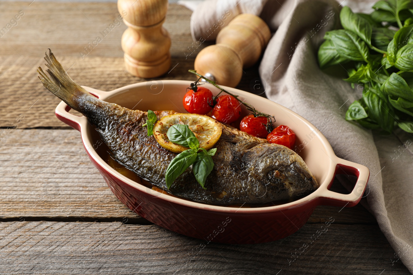 Photo of Delicious roasted dorado fish with tomatoes, basil and lemon on wooden table, closeup