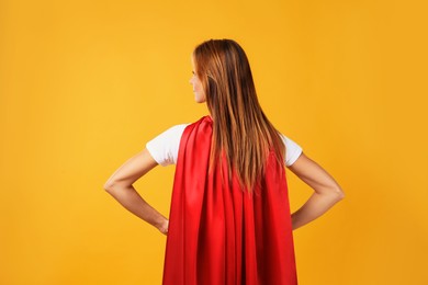 Photo of Woman wearing superhero cape on yellow background, back view