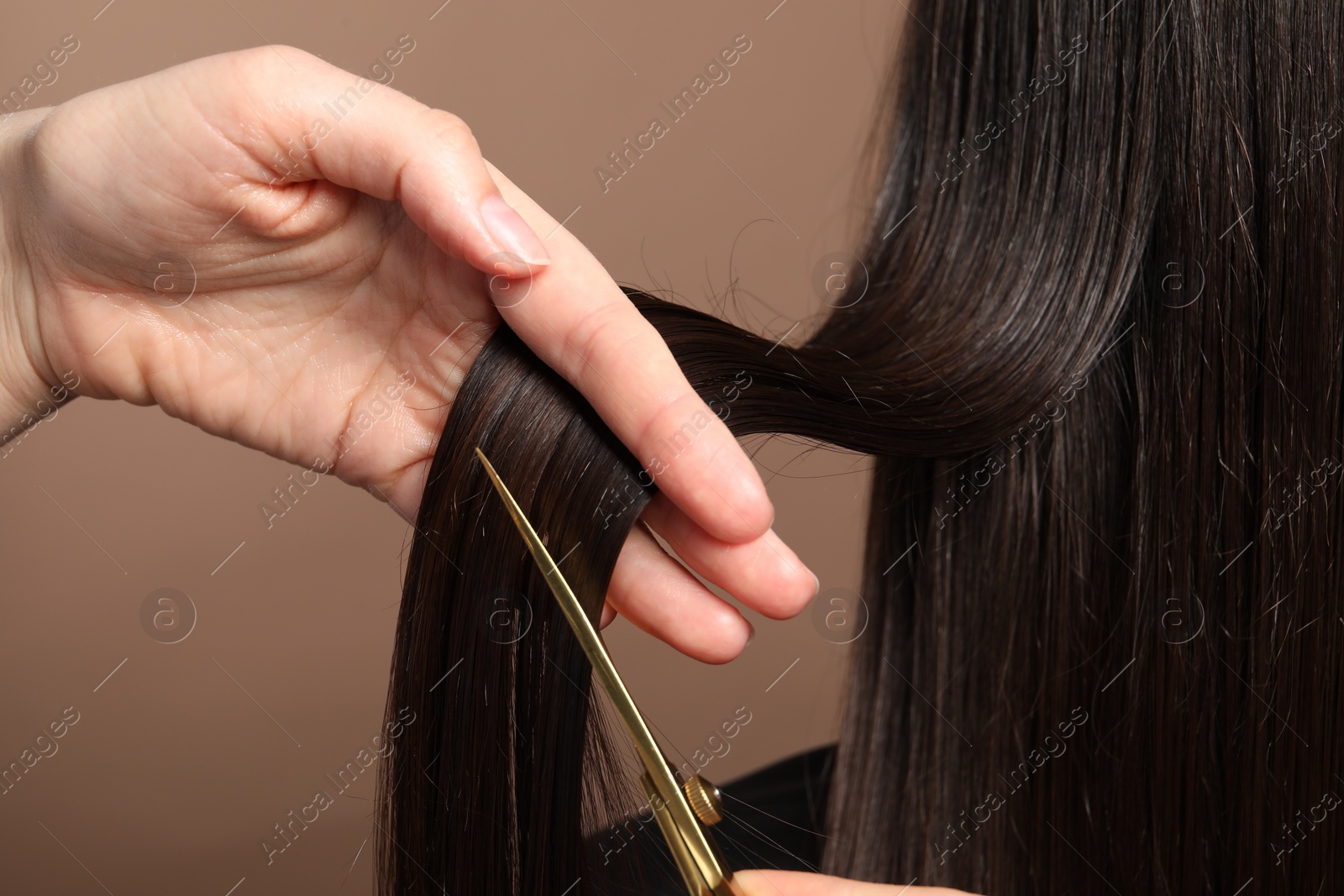 Photo of Hairdresser cutting client's hair with scissors on light brown background, closeup