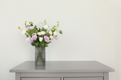 Photo of Bouquet of beautiful Eustoma flowers on chest of drawers near light wall. Space for text