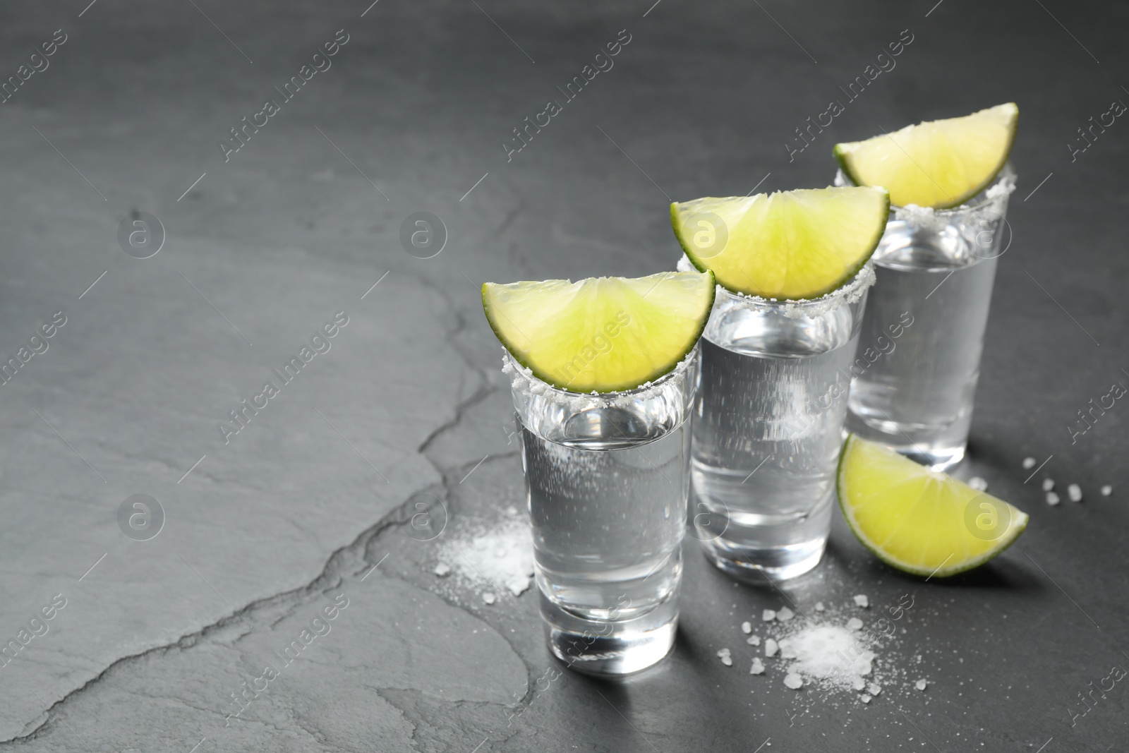 Photo of Mexican Tequila shots, lime slices and salt on black table. Space for text