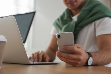 Photo of Freelancer working with laptop and smartphone at table indoors, closeup