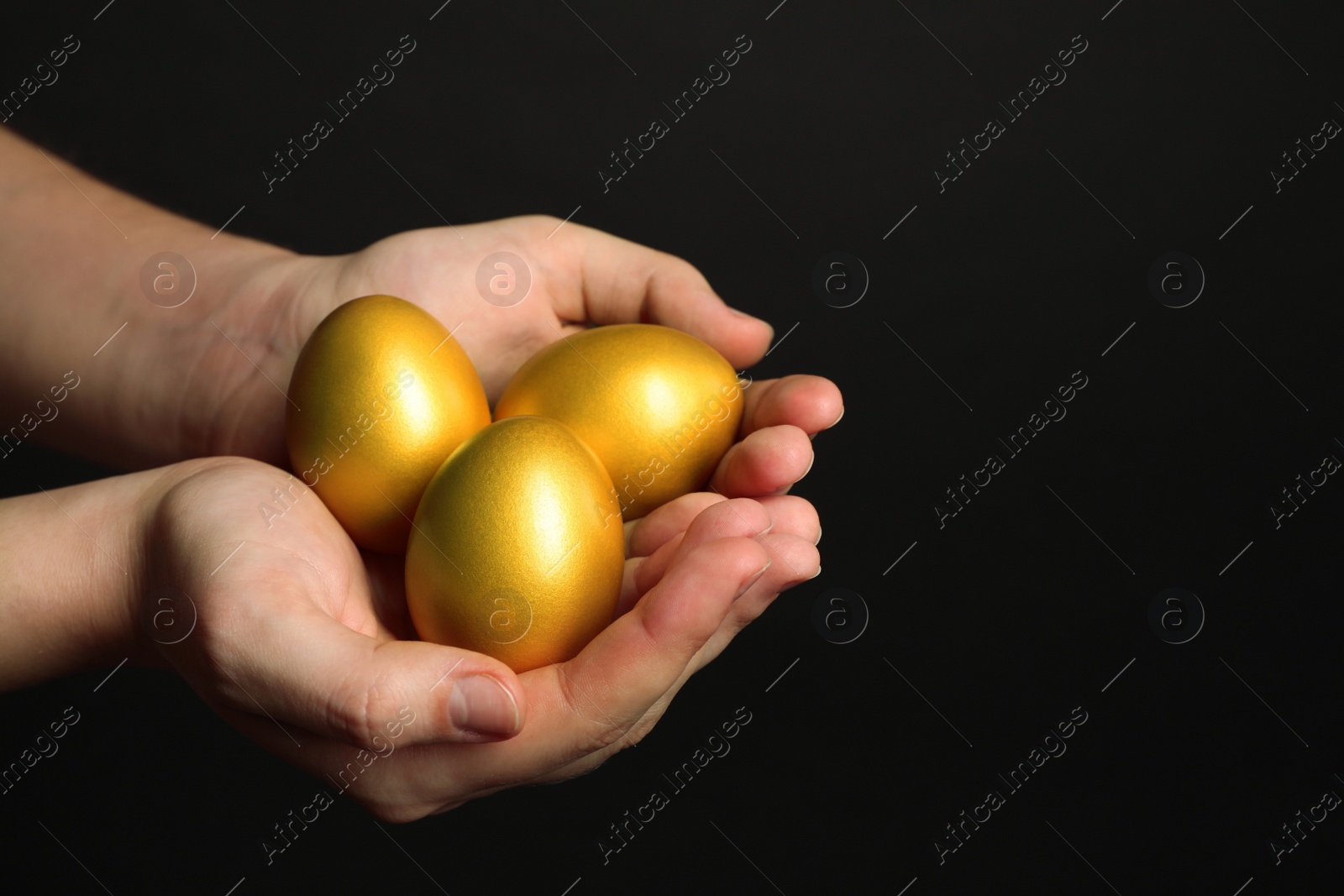 Photo of Woman holding shiny golden eggs on black background, closeup. Space for text