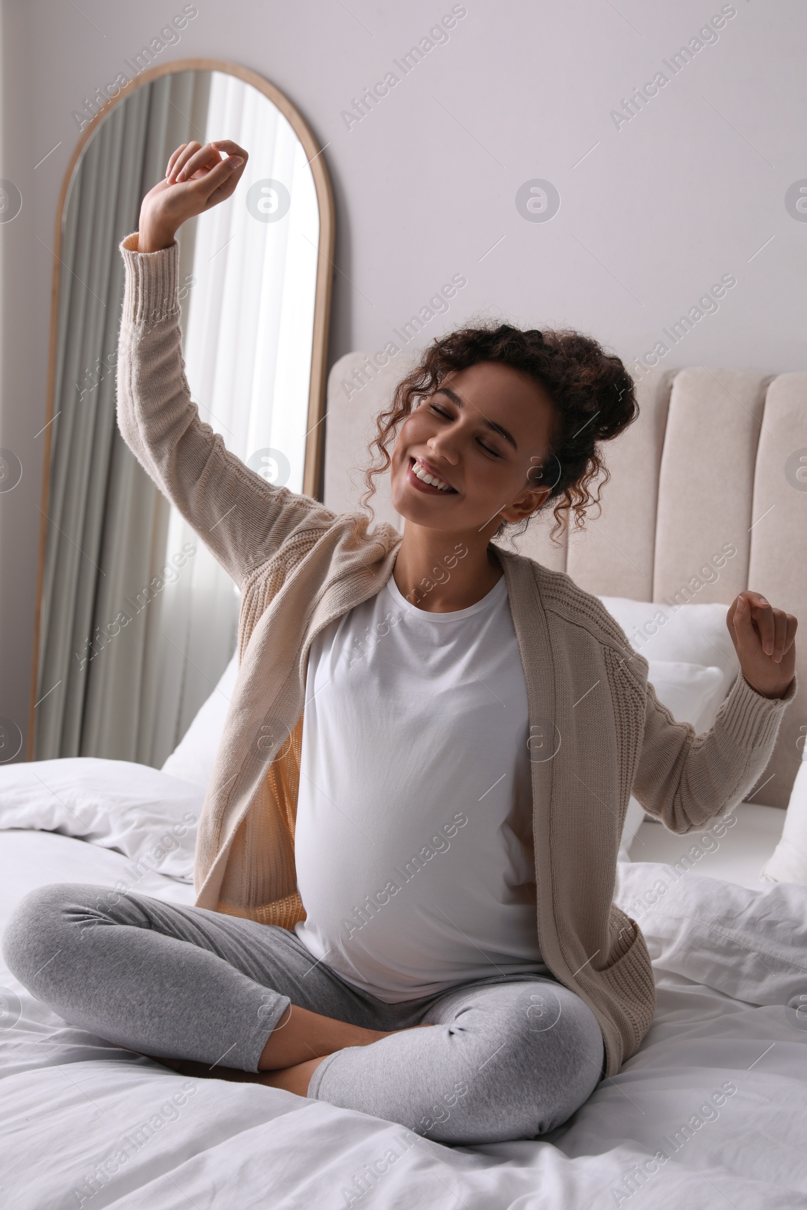 Photo of Excited pregnant young African-American woman sitting on bed at home