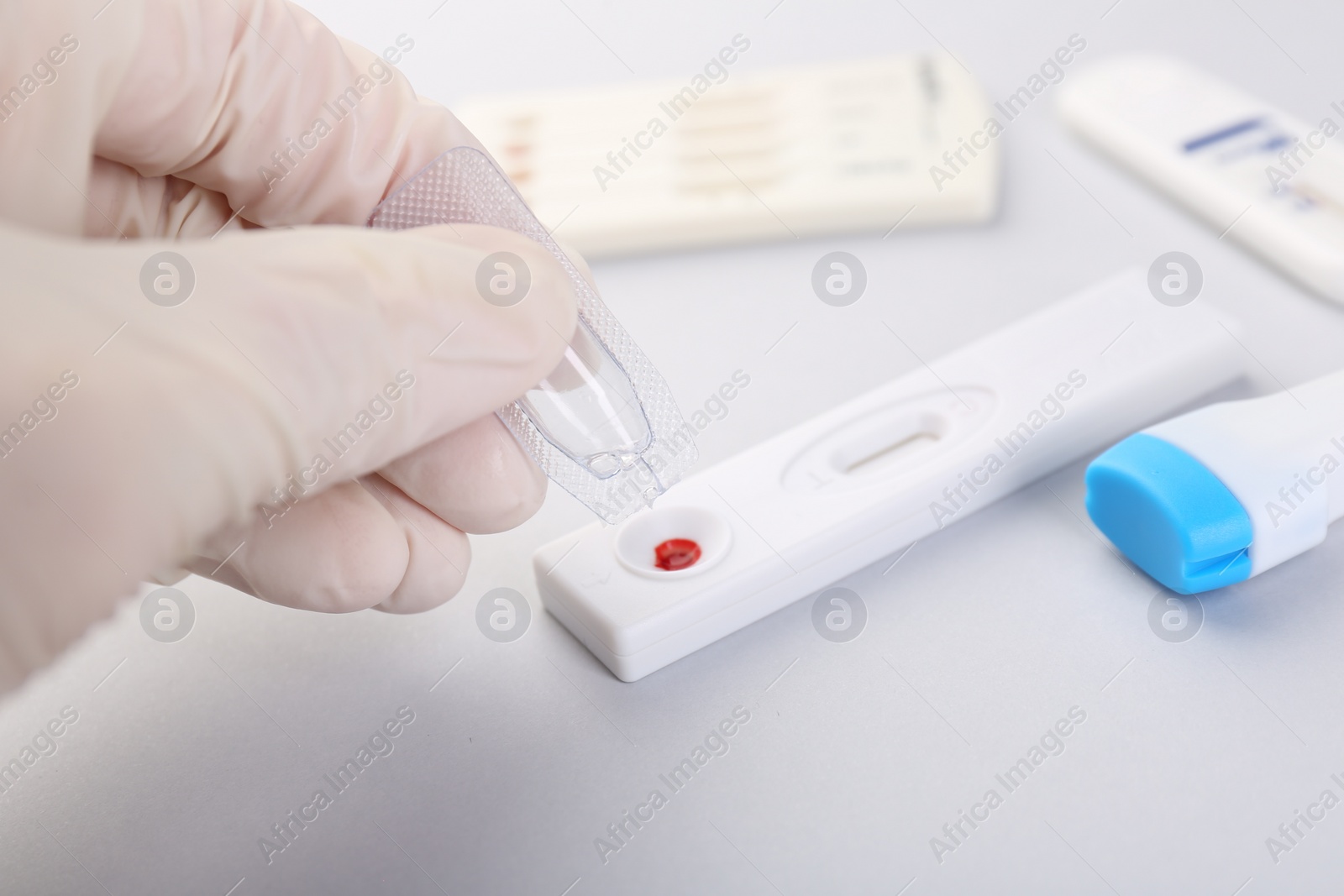 Photo of Doctor dropping buffer solution onto disposable express test cassette on light background, closeup