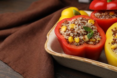 Quinoa stuffed bell peppers and basil in baking dish on wooden table, closeup. Space for text