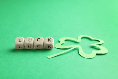 Photo of Word LUCK made with wooden cubes and paper clover leaf on green background