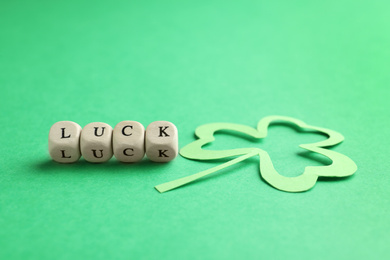 Word LUCK made with wooden cubes and paper clover leaf on green background