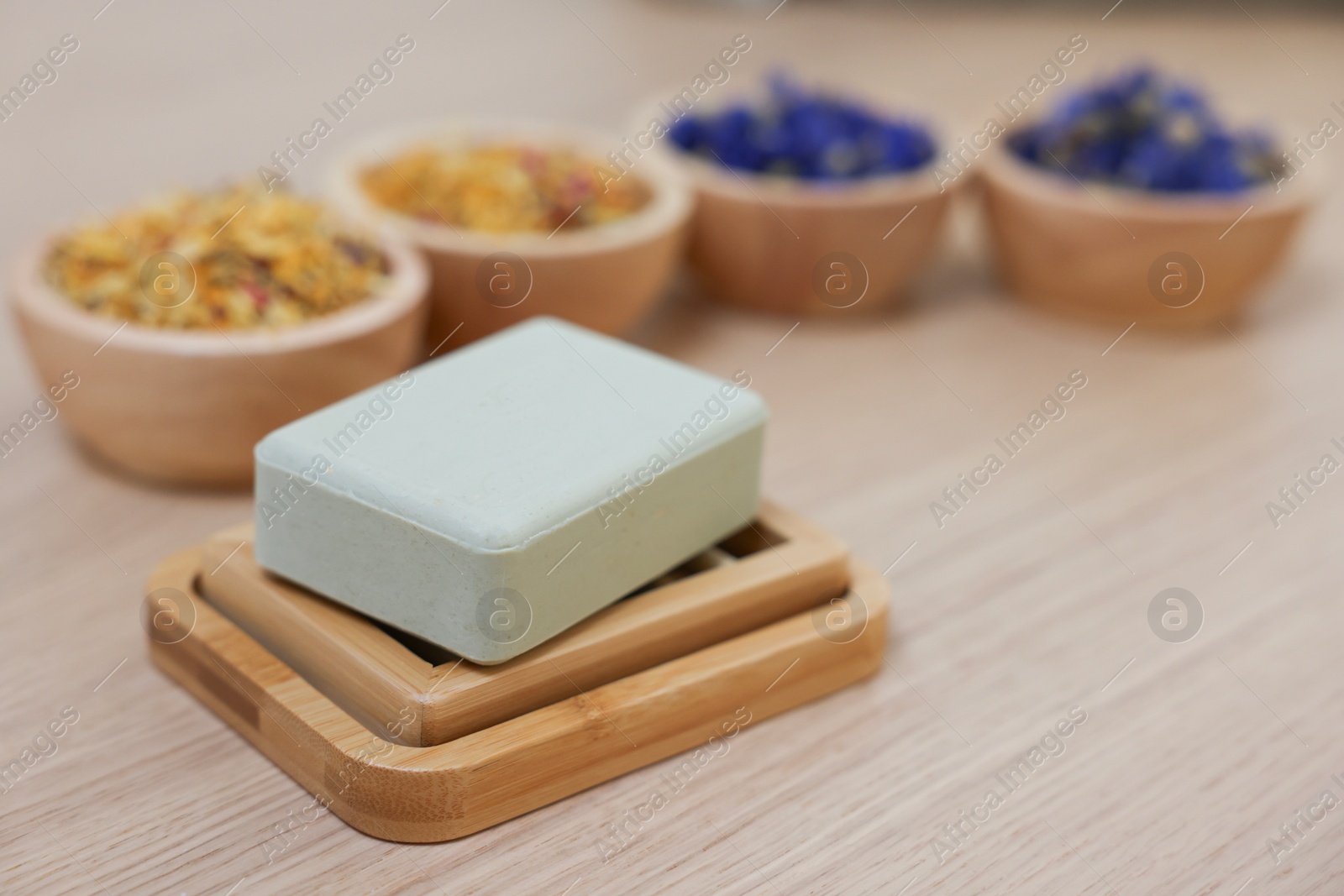 Photo of Soap bar and bowls of dry flowers on light wooden table, space for text. Spa therapy